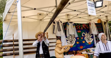 A man playing a bucium at a traditional Moldovan cultural festival stall.