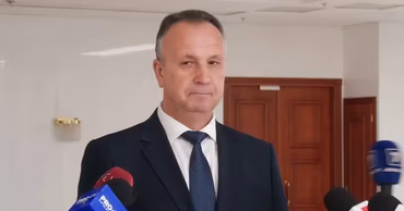 A man in a suit speaking to microphones, likely a government official.