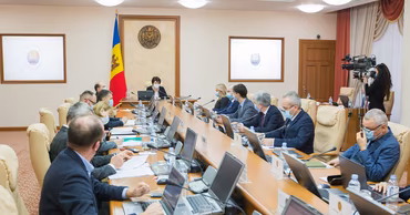 A formal meeting of Moldovan government officials in a conference room with the national flag.