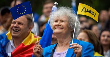 An elderly woman holding European Union and PAS party flags at a public rally.