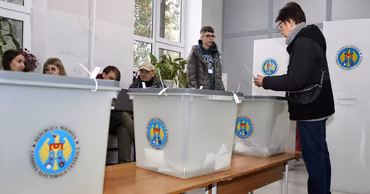 A voter casting a ballot in a Moldovan polling station with official ballot boxes.