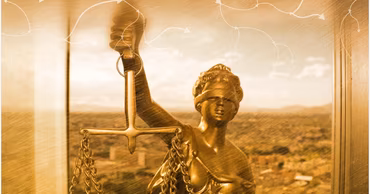 A golden statue of Lady Justice holding scales against a blurred city background.