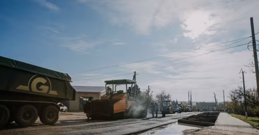 Construction machinery and workers paving a road in a rural area.