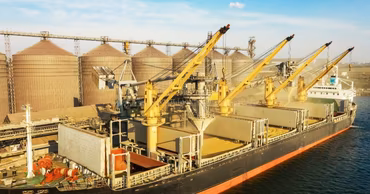 A cargo ship being loaded with grain at a port terminal.