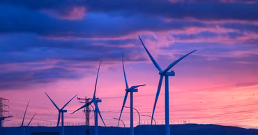 Wind turbines silhouetted against a vibrant sunset sky.