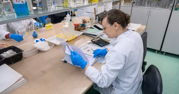 A laboratory technician in a white coat working in a food safety testing facility.