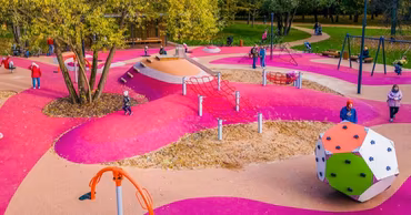 A modern, colorful children's playground with pink rubber flooring and various play equipment.