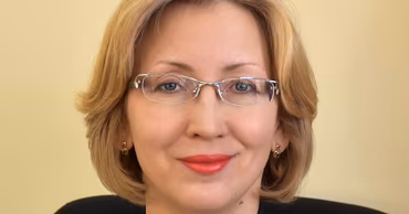 Portrait of Elena Savitski, a woman with blonde hair wearing glasses and a dark blazer.