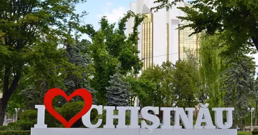 I love Chisinau sign in a park with trees and a building in the background.
