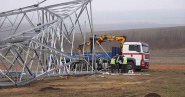 Workers installing a high-voltage electricity pylon in a field.
