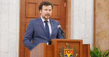 Dan Perciun speaking at a podium with the Moldovan coat of arms.