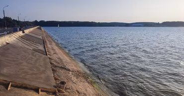 Construction work on a concrete dam reinforcement along a large body of water.
