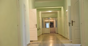 A long, brightly lit corridor inside a hospital building with open doors.