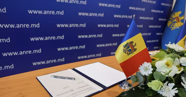 A table with a document, a pen, and the Moldovan flag in front of an ANRE backdrop.
