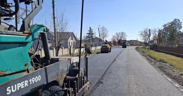 Road construction machinery paving a road in a rural area.