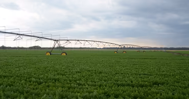 A large center pivot irrigation system operating in a green agricultural field.