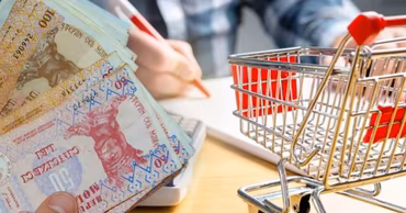 Moldovan Leu banknotes held in hand next to a small shopping cart on a desk.