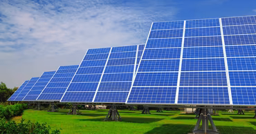 Rows of solar panels installed in a green field under a blue sky.
