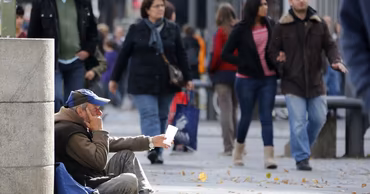 A man sitting on a sidewalk begging for money in a busy city street.