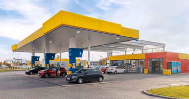 A modern gas station with cars refueling under a yellow canopy.