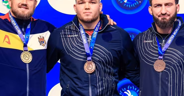 Three Moldovan athletes wearing medals on a podium at a wrestling championship.