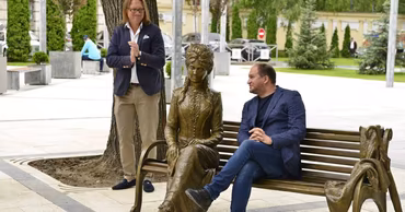 Ion Ceban sitting on a bench next to a bronze statue in a public park in Chisinau.