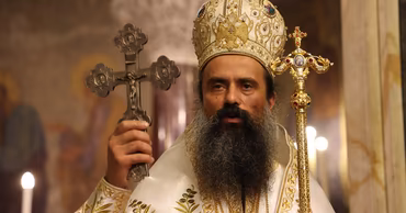Bishop Teofan in religious vestments holding a cross and a pastoral staff during a church service.