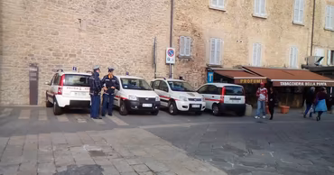 Italian local police officers standing next to their patrol cars in a town square.