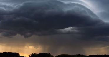 A dark, dramatic storm cloud over a rural landscape with a road.