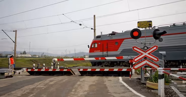 A train passing through a railway crossing with barriers and warning signs in Moldova.