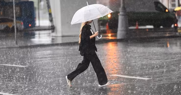 A person walking across a wet street under a transparent umbrella during heavy rain.