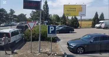 Cars parked near a border crossing point with road signs and a billboard.