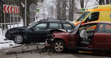 Two damaged cars after a collision on a snowy road with an ambulance in the background.