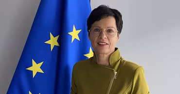 Marta Kos standing in front of a European Union flag.