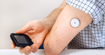 A person using a continuous glucose monitoring sensor on their arm with a reader device.