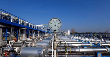 A pressure gauge on a natural gas pipeline facility with industrial pipes in the background.