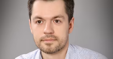 A portrait of Alexei Taran against a grey background.