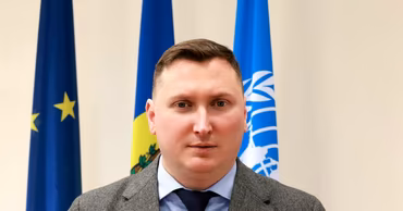 Portrait of Moldovan Ombudsman Ceslav Panico standing in front of flags.