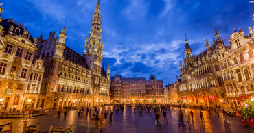 The Grand Place in Brussels at dusk with historic buildings and people walking.