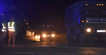 Moldovan military trucks moving on a road at night with a soldier directing traffic.
