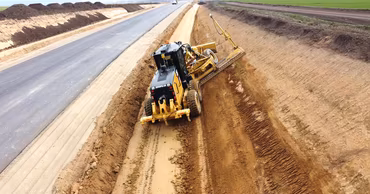 A motor grader working on the side of a newly paved road construction site.