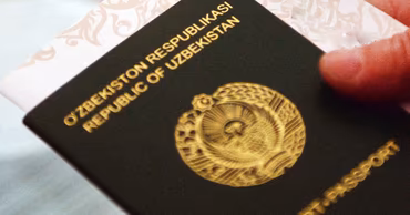 A close-up shot of an Uzbekistan passport held in a hand.