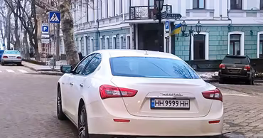 A white Maserati car with Ukrainian license plates parked on a city street.