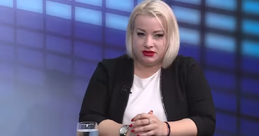 Diana Caraman sitting at a table with a nameplate in a studio setting.