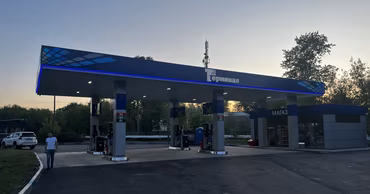 A gas station with fuel pumps and a small shop at sunset.
