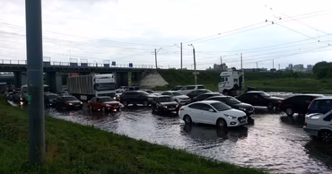 Cars driving through a flooded road under a bridge during heavy rain.