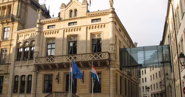 The Chamber of Deputies building in Luxembourg with European and Luxembourgish flags.