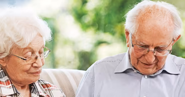 An elderly couple sitting together outdoors.