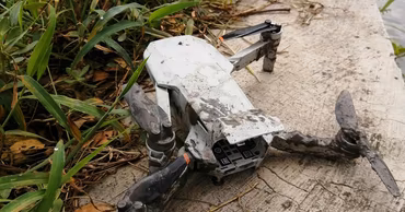 A damaged, mud-covered drone lying on the ground near grass.