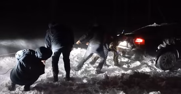 Rescuers pulling a car out of snow at night during severe winter weather.